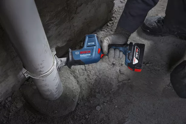 A person wearing safety equipment cuts a plastic pipe with a reciprocating saw.