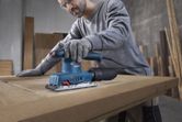 A person wearing safety equipment uses an orbital sander on a wooden door.