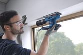 A person wearing safety equipment sands a window frame with an orbital sander.