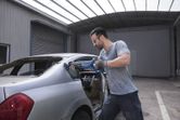 Person wearing safety equipment uses a reciprocating saw to cut a car’s rear window frame.