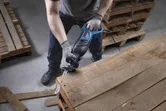 A person wearing safety equipment uses a reciprocating saw to cut a wooden pallet.