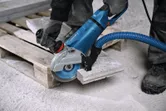 A person wearing safety equipment cuts a concrete slab with a large angle grinder.
