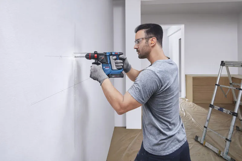 GBH 18V-18 X A person wearing safety equipment drills into a marked wall with a cordless rotary hammer.