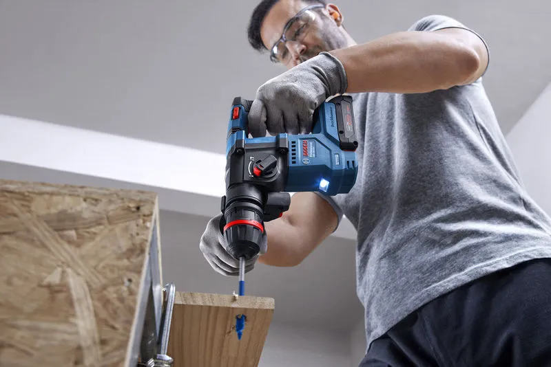 GBH 18V-18 X A person wearing safety equipment drills into wood with a cordless rotary hammer.