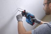 A person wearing safety equipment drills into a wall with a rotary hammer.