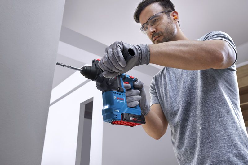 GBH 18V-18 Person wearing safety equipment drills into a wall with a rotary hammer.