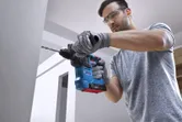 Person wearing safety equipment drills into a wall with a rotary hammer.