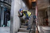 A person wearing safety equipment marks a concrete wall using a laser leveling tool.