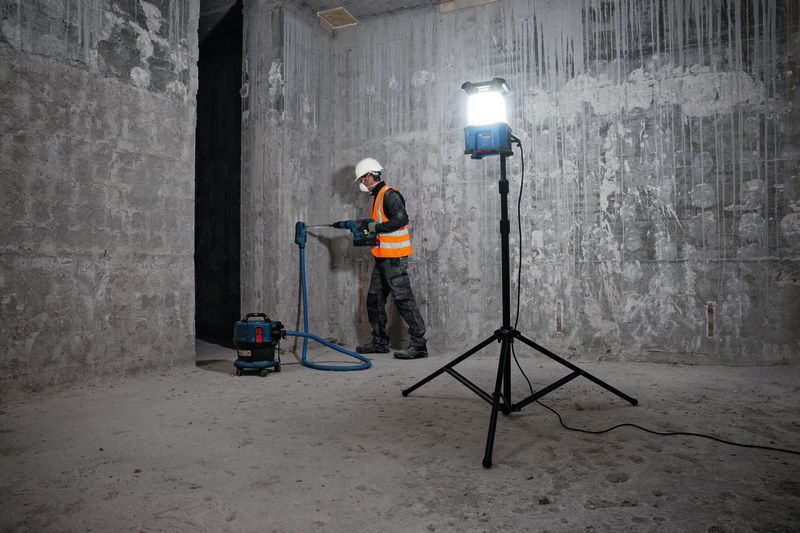 A person wearing safety equipment drills into a concrete wall in a construction area.