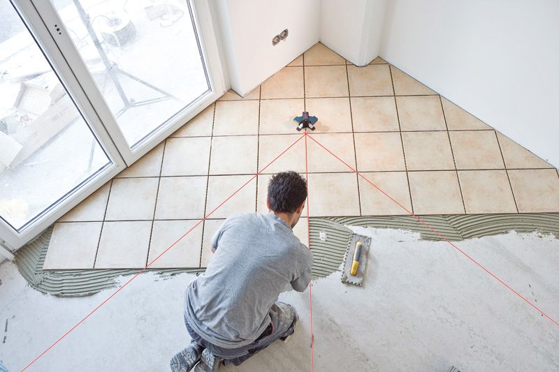 A person kneels on the floor using a tile laser leveling tool.