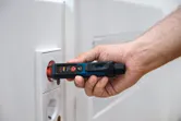 A person uses a non-contact voltage tester near an electrical socket.