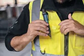 Person wearing safety equipment places a non-contact voltage tester in a vest pocket.