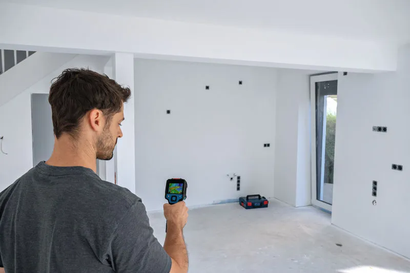 Person uses a thermo camera to inspect a white-walled room under construction.