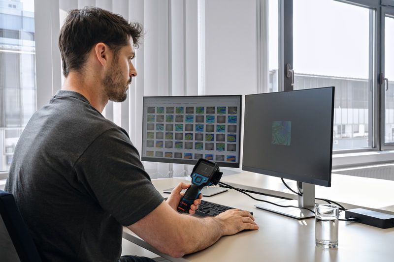 Person analyzing thermal images on dual monitors using a thermo camera at a desk.