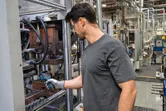 A person wearing safety equipment inspects machinery with a thermo camera in a factory.