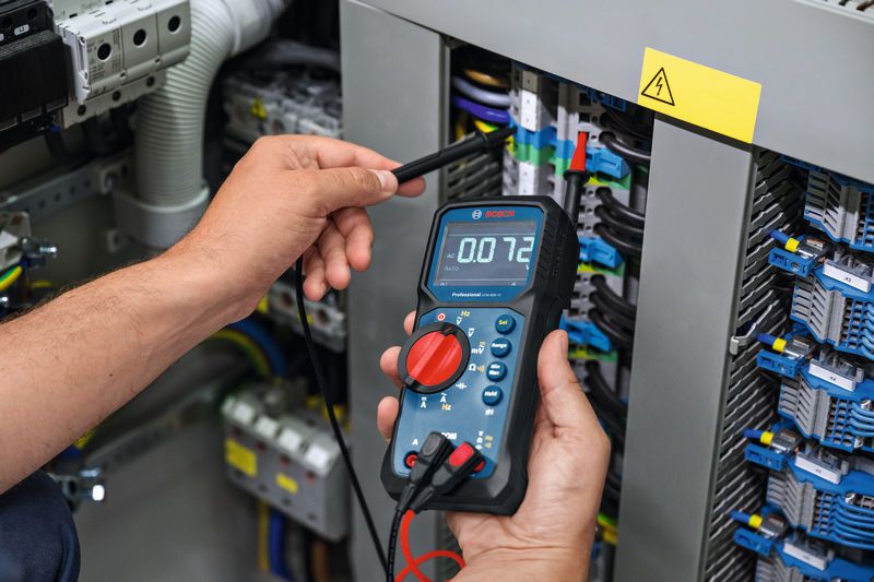 Person measures voltage on electrical panel using a digital multimeter.