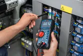 Person measures voltage on electrical panel using a digital multimeter.
