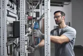 A person wearing safety equipment uses a cordless ratchet wrench on a metal rack.
