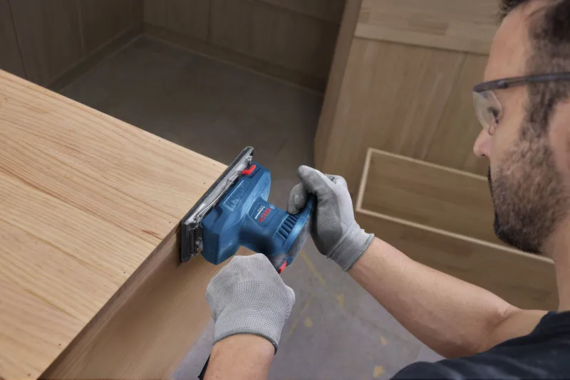 A person wearing safety equipment sands a wooden surface with an orbital sander.