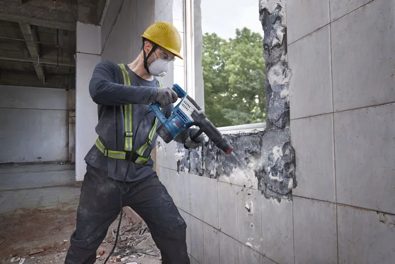 GSH 5 HX A worker wearing safety equipment uses a demolition hammer to break a tiled wall.