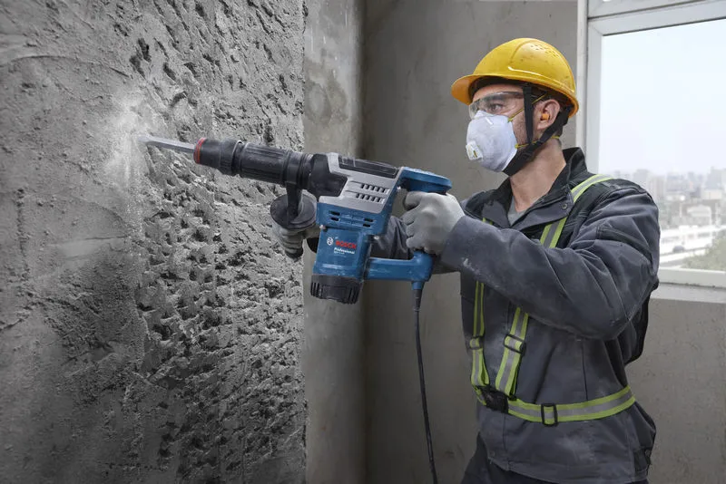 GSH 5 HX A person wearing safety equipment uses a demolition hammer to break a concrete wall.