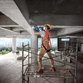 A person wearing safety equipment uses a demolition hammer on a concrete beam.