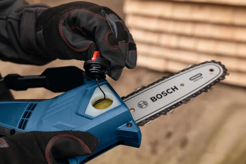 A person wearing safety equipment refills oil in a cordless pruner saw.