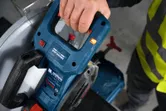 A person wearing safety equipment operates a metal cut-off saw.