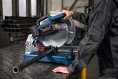 A person wearing safety equipment operates a metal cut-off saw cutting a pipe.