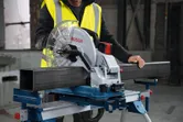 A person wearing safety equipment operates a metal cut-off saw to cut a steel beam.