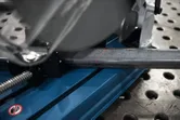 Metal cut-off saw with a red guide line cutting a steel bar on a perforated workbench.