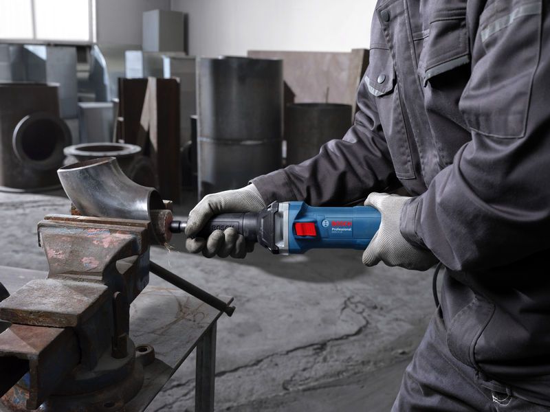 GGS 5 LS A person wearing safety equipment uses a straight grinder to grind a metal pipe in a workshop.
