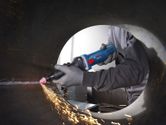A person wearing safety equipment uses a straight grinder to smooth the inside of a metal pipe.