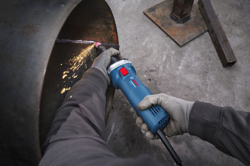 GGS 5 LS A person wearing safety equipment uses a straight grinder to grind the edge of a metal pipe.
