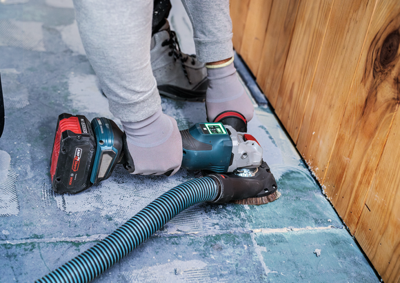 A person wearing safety equipment sands a concrete floor near a wooden wall.