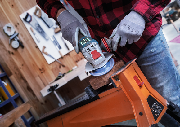 Person wearing safety equipment uses an angle grinder to sand wood clamped to a workbench.