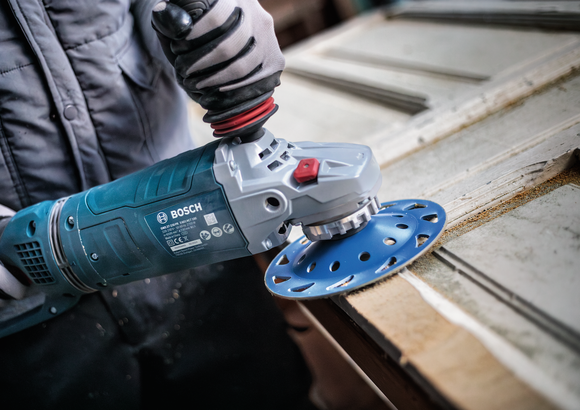 Person wearing safety equipment uses an angle grinder to sand a wooden door surface.