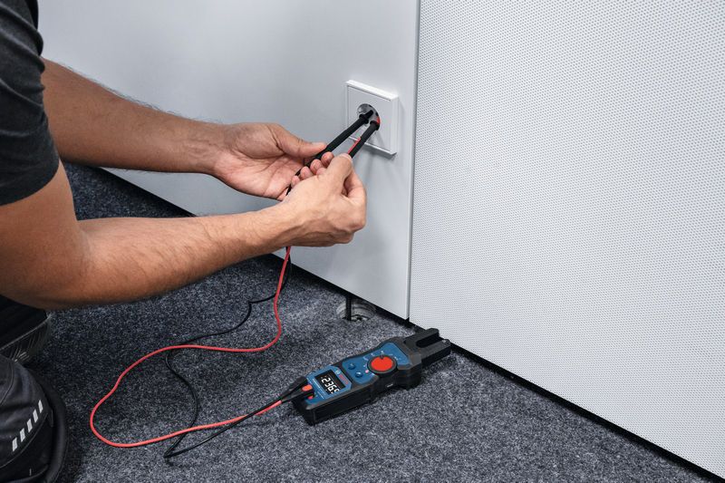 Person uses a fork meter to measure voltage at an electrical outlet.