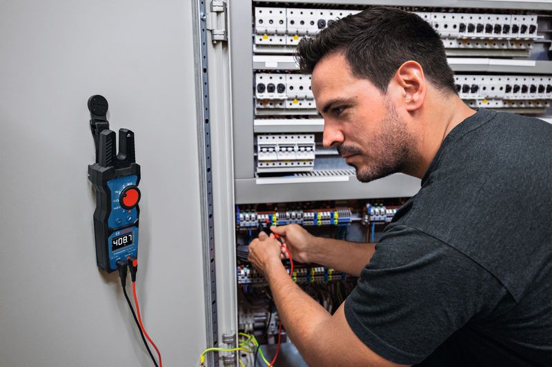 A person checks electrical wires in a control panel using a digital multimeter.