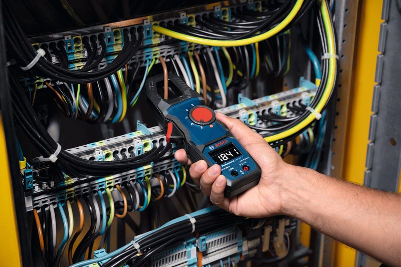 A person uses a clamp meter to measure current in an electrical control panel.
