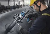 A person wearing safety equipment tightens bolts on industrial piping with a cordless impact wrench.