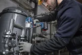 A person wearing safety equipment uses a cordless impact wrench on industrial piping.