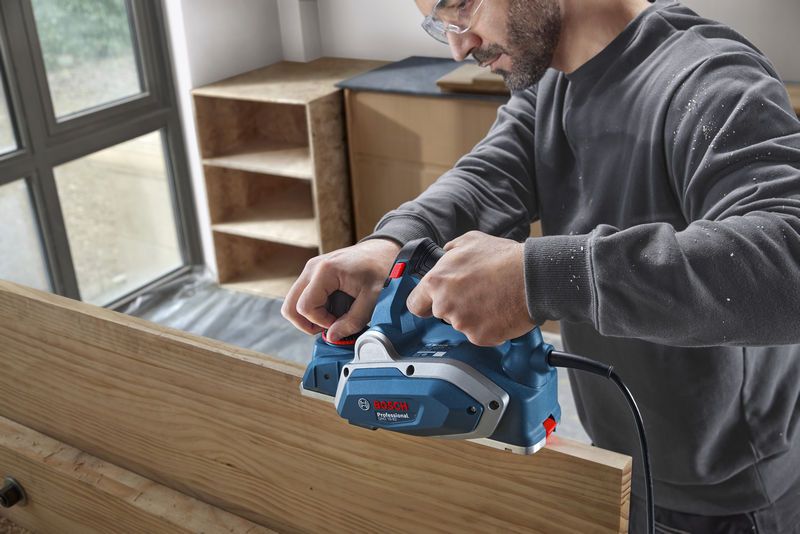 GHO 16-82 A person wearing safety equipment smooths a wooden board using an electric planer.