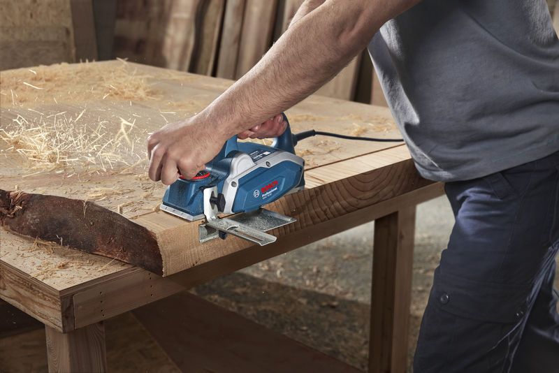 GHO 16-82 A person uses an electric planer to smooth a wooden plank on a workbench.