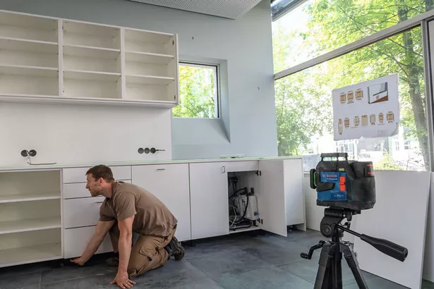 GLL 90-33 XG Person installing kitchen cabinets uses a laser leveling tool on a tripod for alignment.