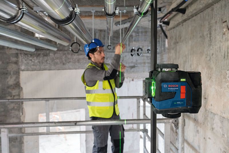 A person wearing safety equipment aligns pipes using a laser leveling tool.