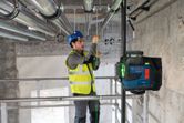 A person wearing safety equipment aligns pipes using a laser leveling tool.
