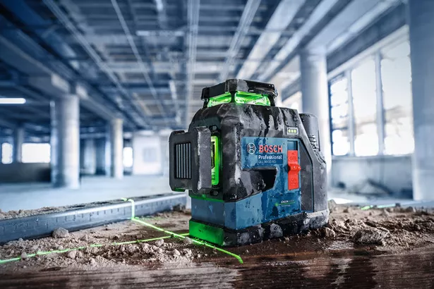 GLL 90-33 XG Laser leveling tool projecting green lines on a dusty floor at a construction site.