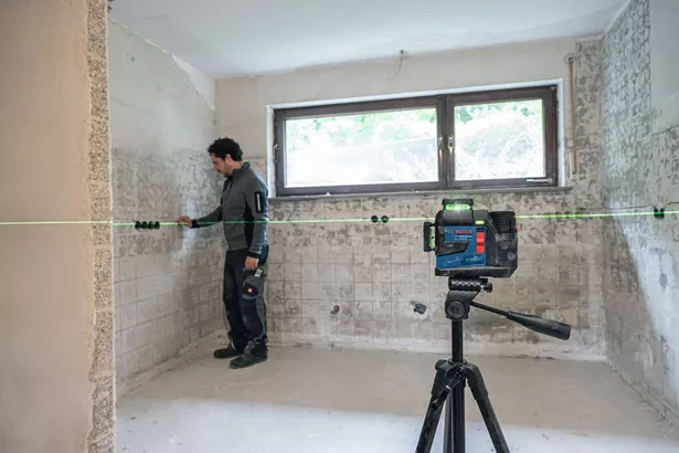 GLL 90-33 XG Person wearing safety equipment aligns wall features using a laser leveling tool in a tiled room.