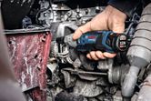 A person uses a cordless ratchet wrench to tighten a bolt on an engine.